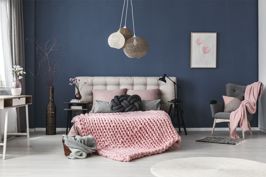 Quarto com a parede azul marinho e cama com colcha rosa centralizada.